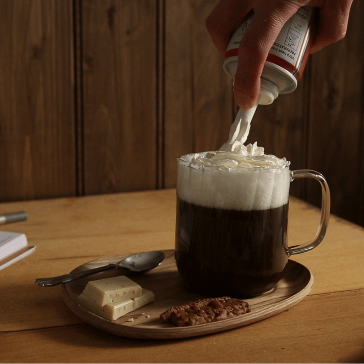 Someone spraying whipped cream on hot chocolate GIF