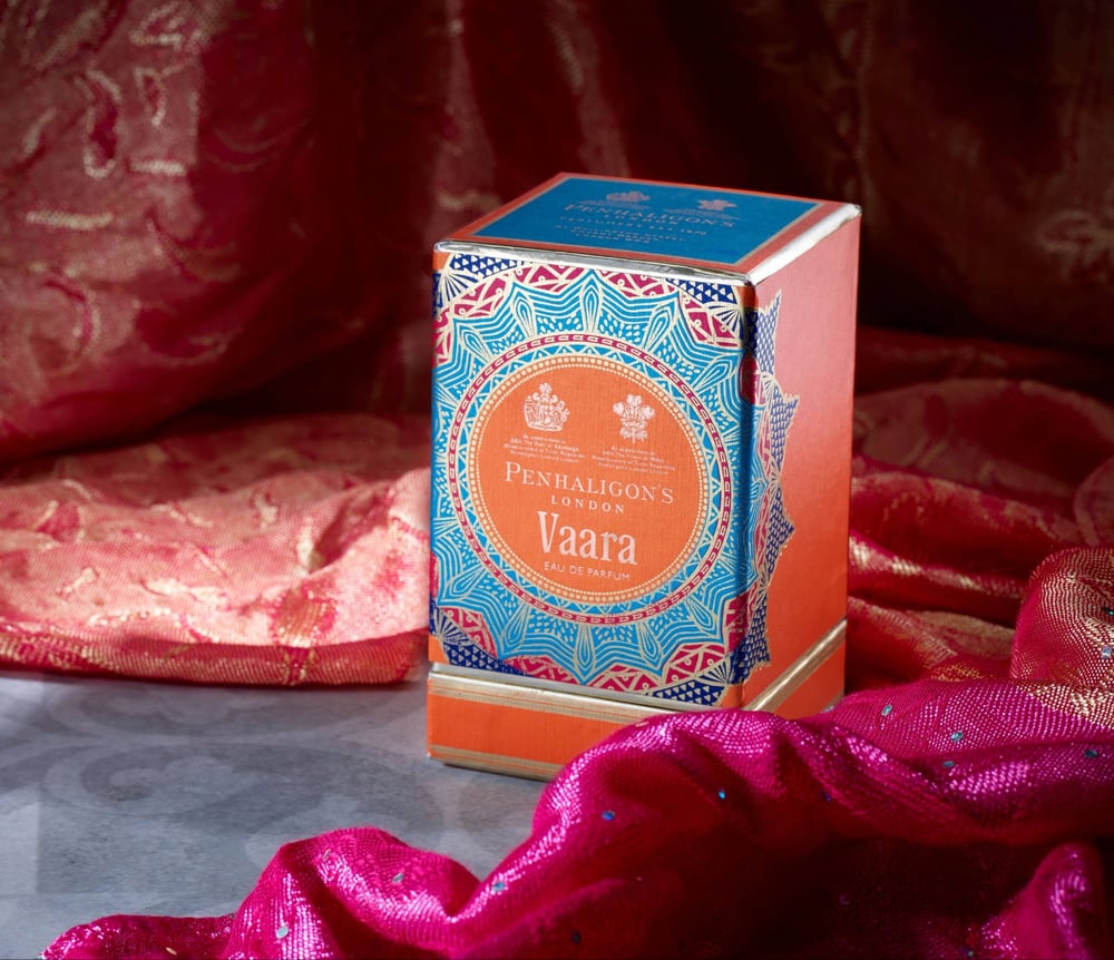 A metallic blue, pink and orange Penhaligon's fragrance box on a piece of shiny pink fabric